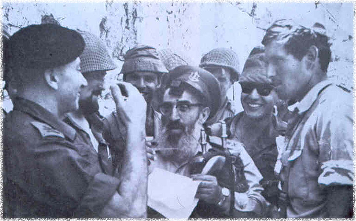 The Chief Rabbi of the Israel Defence Forces, Shlomo Goren, arrives at the liberated Western Wall. To his right are General Uzi Narkiss and HaRav Menachem Cohen. To his far left is the fellow paratrooper who planted the Israeli flag upon the Temple Mount - declaring Jewish sovereignty over the Mount, ending 1,897 years of exile.